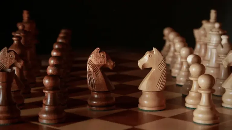Twee houten paarden die elkaar aankijken op een schaakbord, als symbolische header voor een artikel over de beweging en kracht van het paard in schaken.