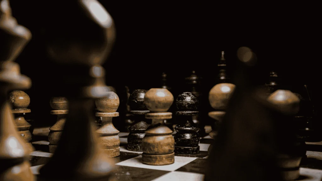 Houten schaakstukken op een bord met sterke licht‑donker contrasten, voor uitleg over schaakstrategieën en eindspelen.